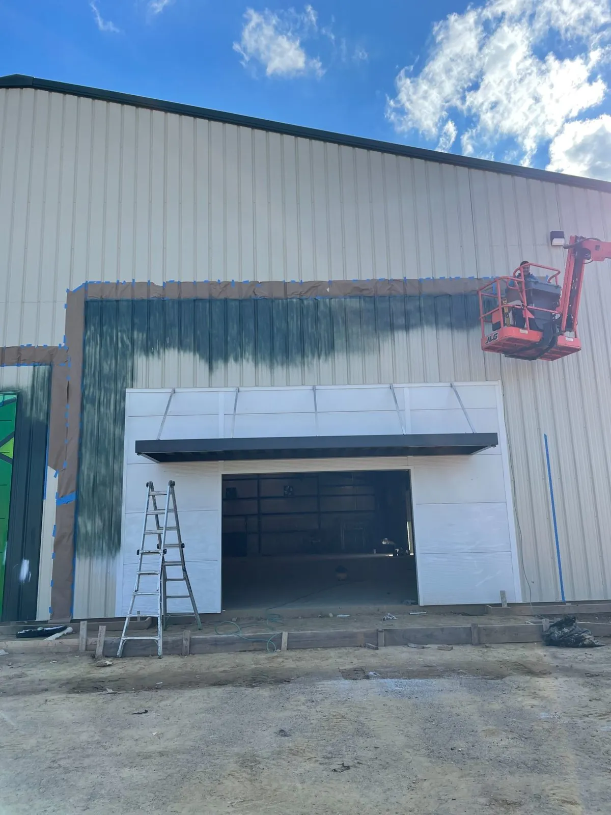 Exterior metal siding being masked and coated during commercial building construction