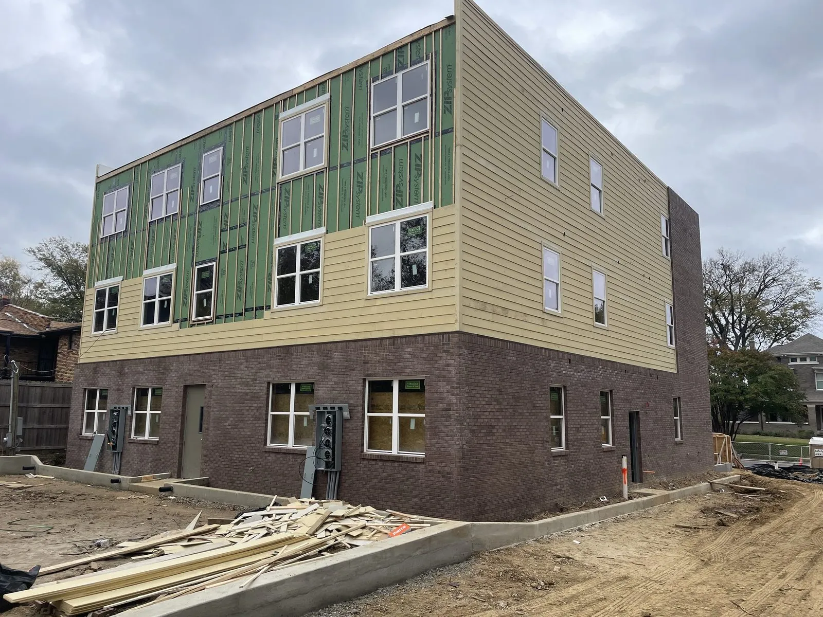 Multifamily building in progress — brick base complete, panel siding going on, windows installed